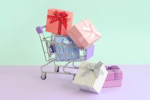 Small gift boxes of different colors with ribbons lies in shopping cart on a violet and blue pastel background photo