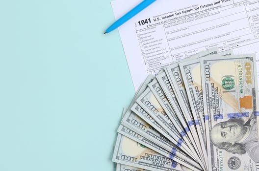 1041 tax form lies near hundred dollar bills and blue pen on a light blue background. US Income tax return for estates and trusts photo