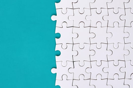 Fragment of a folded white jigsaw puzzle on the background of a blue plastic surface. Texture photo with copy space for text