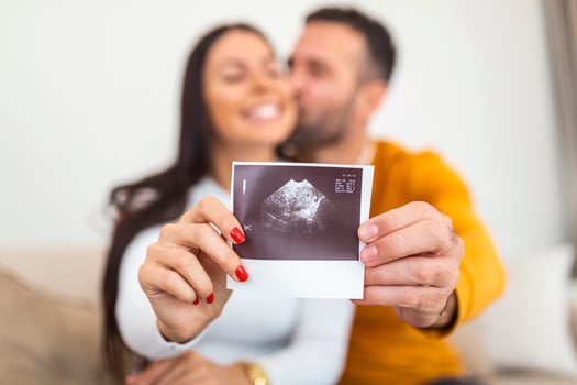 Happy pregnant woman with baby ultrasound photo embracing with her husband. Woman is holding an X-ray image of a fetus