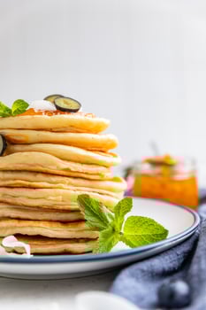 Stack of fluffy pancakes with orange jam, blueberries, coconut chips and mint, light background. Traditional breakfast. High key photography. photo