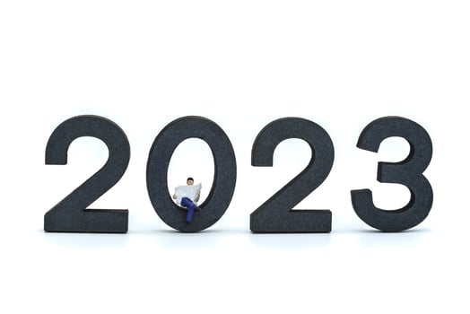 2023 Business New Year Concept. Closeup of businessman miniature figures sitting and reading a newspaper on wooden number on white background. photo