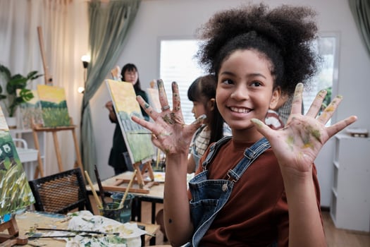 African American girl shows hand messed up with acrylic colors, joy, and fun learns with student children in art studio of an elementary classroom, creative painting with skills in school education. photo