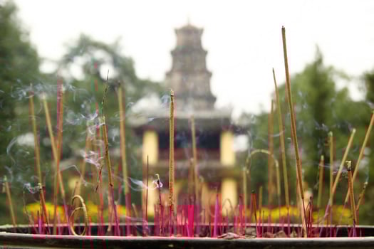 Aroma sticks near to the temple on a background of garden with yellow flowers. Hue, Vietnam. photo