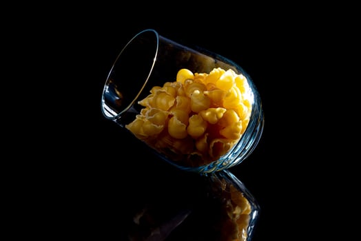 raw pasta in glass jar, wine glass. in bucket. raw pasta on black background. front view raw pasta, dropped from hand, place for text, yellow long spaghetti straws, photo
