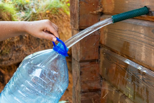 collecting natural spring water in a 5-liter plastic bottle, filling the bottle with fresh clean drinking water photo