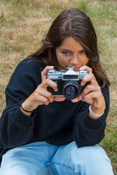 Cute teen girl with a camera, a girl taking pictures on a retro vintage camera on the grass in the park, a hobby concept photo