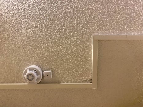 White plastic small fire detector smoke detector with alarm on the ceiling in the entrance. The background photo