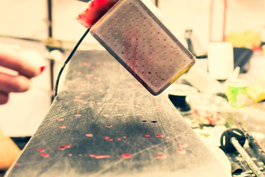 Ski repair shop employee workman melts drops red wax on snowboard with special wax iron. Ski snowboard waxing service and preparation. Step by step guide photo
