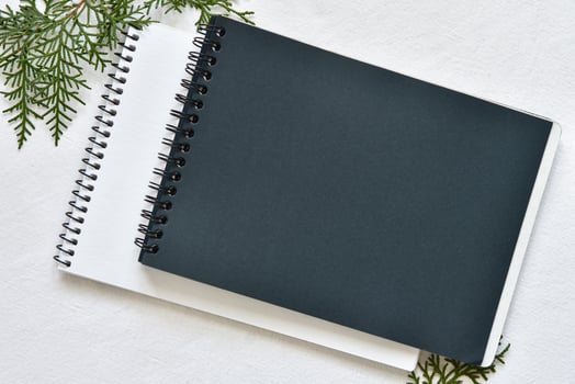 black and white sketchbook on a spring lying on a linen tablecloth with sprigs of green thuja photo