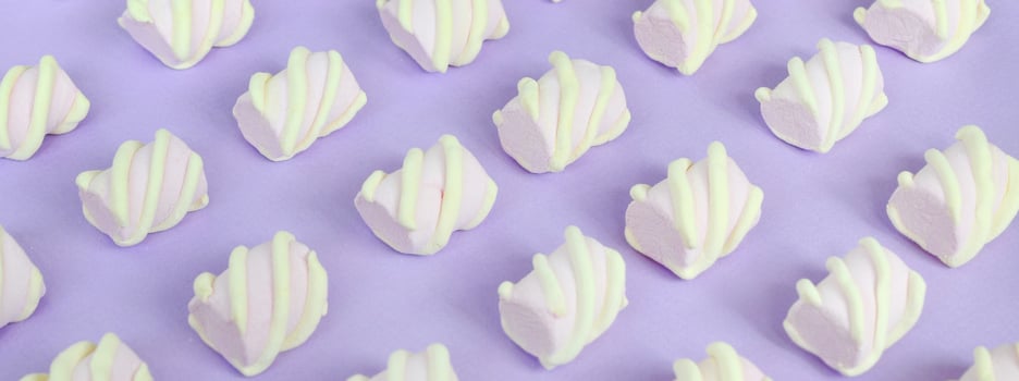 Colorful marshmallow laid out on violet paper background. pastel creative textured pattern. Perspective macro shot photo