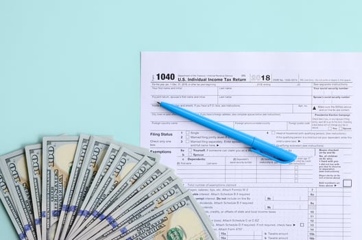 1040 tax form lies near hundred dollar bills and blue pen on a light blue background. US Individual income tax return photo