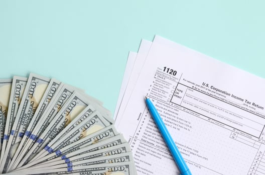 1120 tax form lies near hundred dollar bills and blue pen on a light blue background. US Corporation income tax return photo