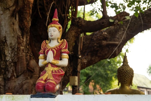 Small stone red and gold statue Buddha near to temple on a background of tree. Chiang Mai, Thailand. photo