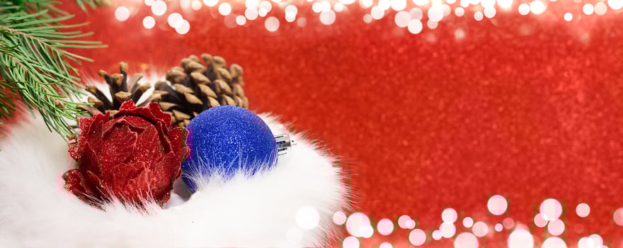 Christmas balls with cones in fur gift bag with fir branch on red blurred background with white bokeh. Banner, concept of shopping, sales. New Year. Copy space photo
