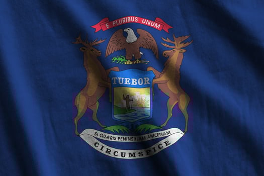 Michigan US state flag with big folds waving close up under the studio light indoors. The official symbols and colors in banner photo