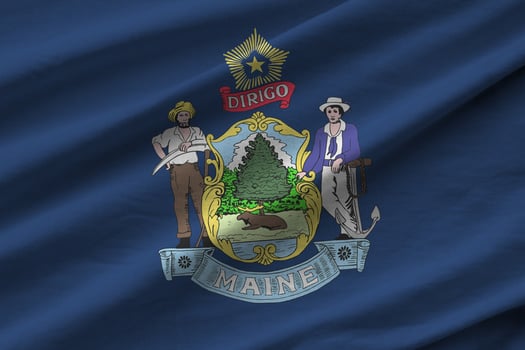 Maine US state flag with big folds waving close up under the studio light indoors. The official symbols and colors in banner photo
