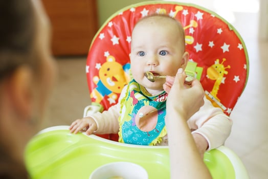 Mom feeds funny baby from a spoon . child eats in a highchair photo