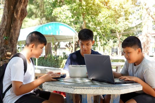 Three Asian boys sit on a marble table under a tree. Use laptop, tablet, to search for learning information from media on the Internet. It is self-learning outside the classroom. photo