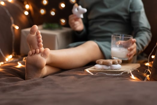 Close up Child bare feet, glass of milk cinnamon eggnog,Christmas sweets ginger cookies,craft paper box gift. Kid Christmas morning breakfast. Egg-nog photo