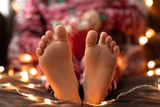 Close up Child bare feet Kid in red Christmas pajamas hold mug cup striped green red candy Christmas canes bokeh lights background. New year photo