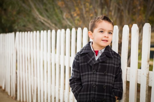 Young Mixed Race Boy Waiting For School Bus Along Fence Outside. photo