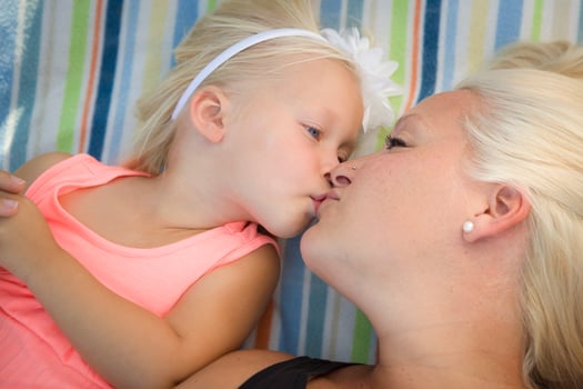 Little Girl Laying on Blanket Kisses Her Mommy photo