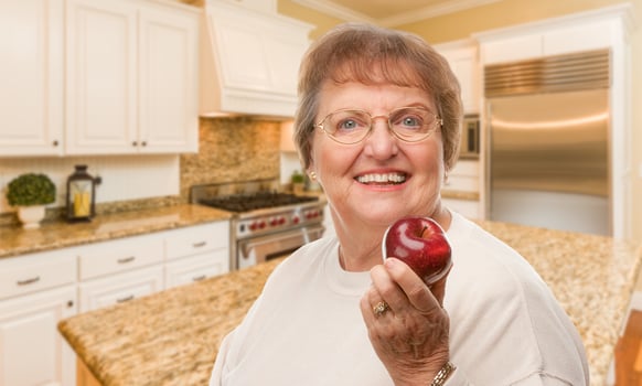 Happy Senior Adult Woman with Red Apple Inside Kitchen. photo