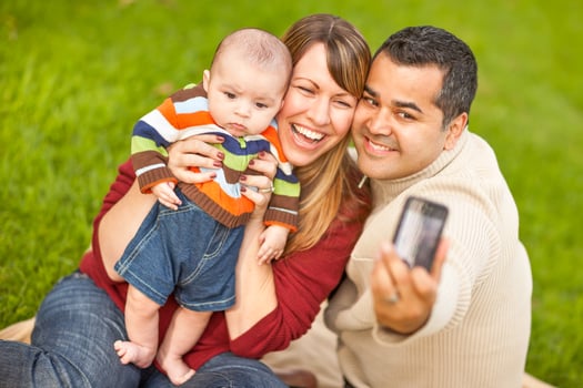 Happy Mixed Race Parents and Baby Boy Taking Self Portraits at the Park photo