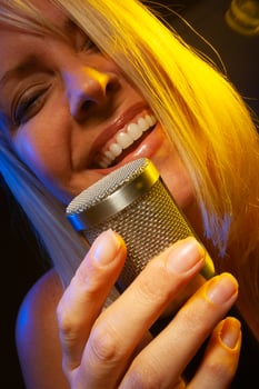 Female vocalist under gelled lighting sings with passion into condenser microphone. photo