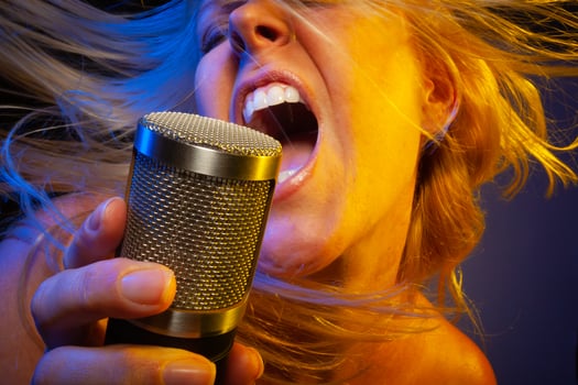 Female vocalist under gelled lighting sings with passion into condenser microphone. photo