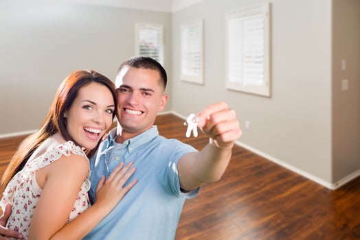 Young Military Couple Showing Off House Keys in Empty Room of New Home photo