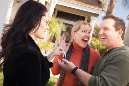 Hispanic Female Real Estate Agent Handing Keys to Excited Couple photo