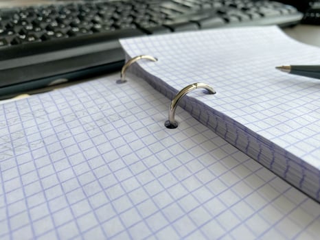 One paper notepad with spiral binder and blank sheets near black plastic pen lies of blue office table. Top view. Copy space for photo
