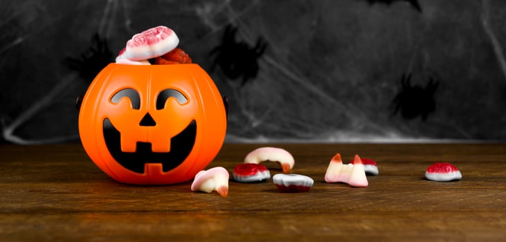 Halloween picture with trick or treat concept.Jack'o'lantern shaped candy bowl with delicios scary sweets on dark background with spiderweb photo