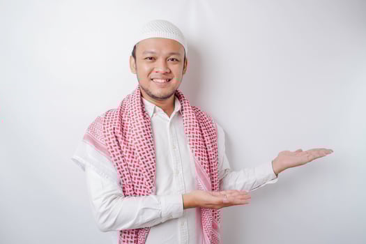 Excited Asian Muslim man pointing at the copy space beside him, isolated by white background photo