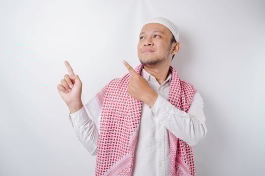 Excited Asian Muslim man pointing at the copy space beside him, isolated by white background photo