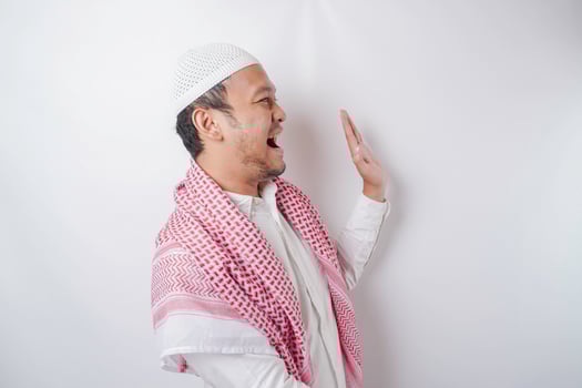 Excited Asian Muslim man pointing at the copy space beside him, isolated by white background photo