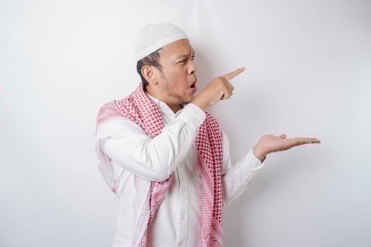 Shocked Asian Muslim man pointing at the copy space beside him, isolated by white background photo