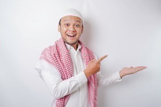 Excited Asian Muslim man pointing at the copy space beside him, isolated by white background photo
