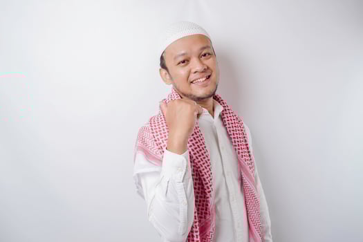 Excited Asian Muslim man pointing at the copy space beside him, isolated by white background photo