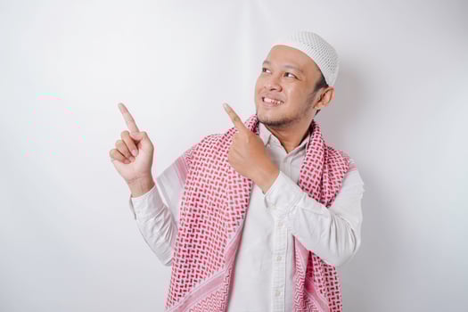 Excited Asian Muslim man pointing at the copy space beside him, isolated by white background photo