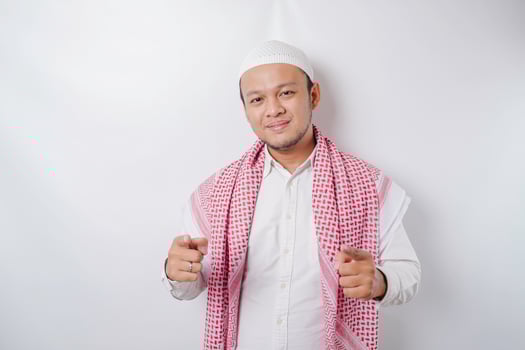 Young Asian Muslim man standing over isolated white background pointing fingers to camera with happy face. Good energy and vibes. photo