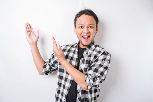 Smiling Asian man wearing tartan shirt is pointing at the copy space on top of him, isolated by white background photo