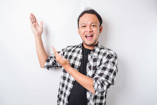 Smiling Asian man wearing tartan shirt is pointing at the copy space on top of him, isolated by white background photo