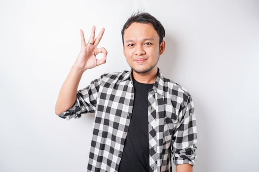Excited Asian man wearing tartan shirt giving an OK hand gesture isolated by a white background photo