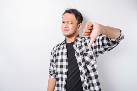 Disappointed Asian man wearing tartan short gives thumbs down hand gesture of approval, isolated by white background photo