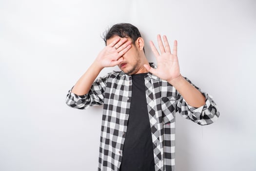 Young scared Asian man isolated on white background, looks depressed, face covered by fingers frightened and nervous. photo