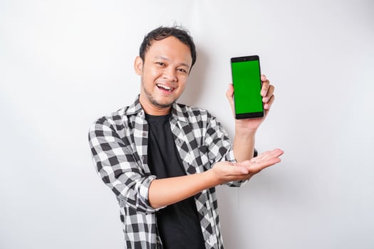 A portrait of a happy Asian man is smiling while showing copy space on his phone, isolated by white background photo