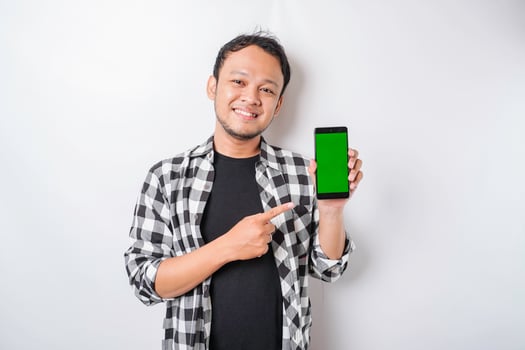 A portrait of a happy Asian man is smiling while showing copy space on his phone, isolated by white background photo